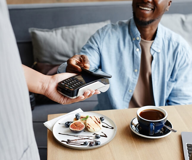 Homem sorrindo e pagando a conta com o celular Homem sorrindo e pagando a conta com o celular
